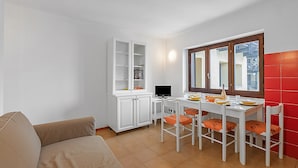 Ein kompakter Wohnbereich mit Sofa, Esstisch, Stühlen, einem weißen Schrank und einem Fenster mit Aussicht.