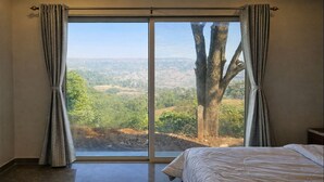 A bedroom with a large sliding glass door leading to a scenic view of a tree and landscape. - Royal Hilltop Villa Private 5BHK Lush Green Valley View Food Caretaker WiFi (Panchgani)
