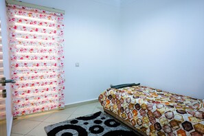 Ein Schlafzimmer mit einem Bett, einem gemusterten Teppich und einer Tür mit floralem Rollo.