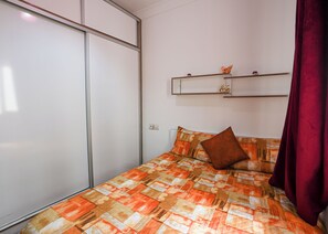 A bedroom with a bed, a red curtain, a white wardrobe, and a shelf with decorative items. - ABOUAB GUELIZ 2 APARTMENT MARRAKECH (Marrakech)