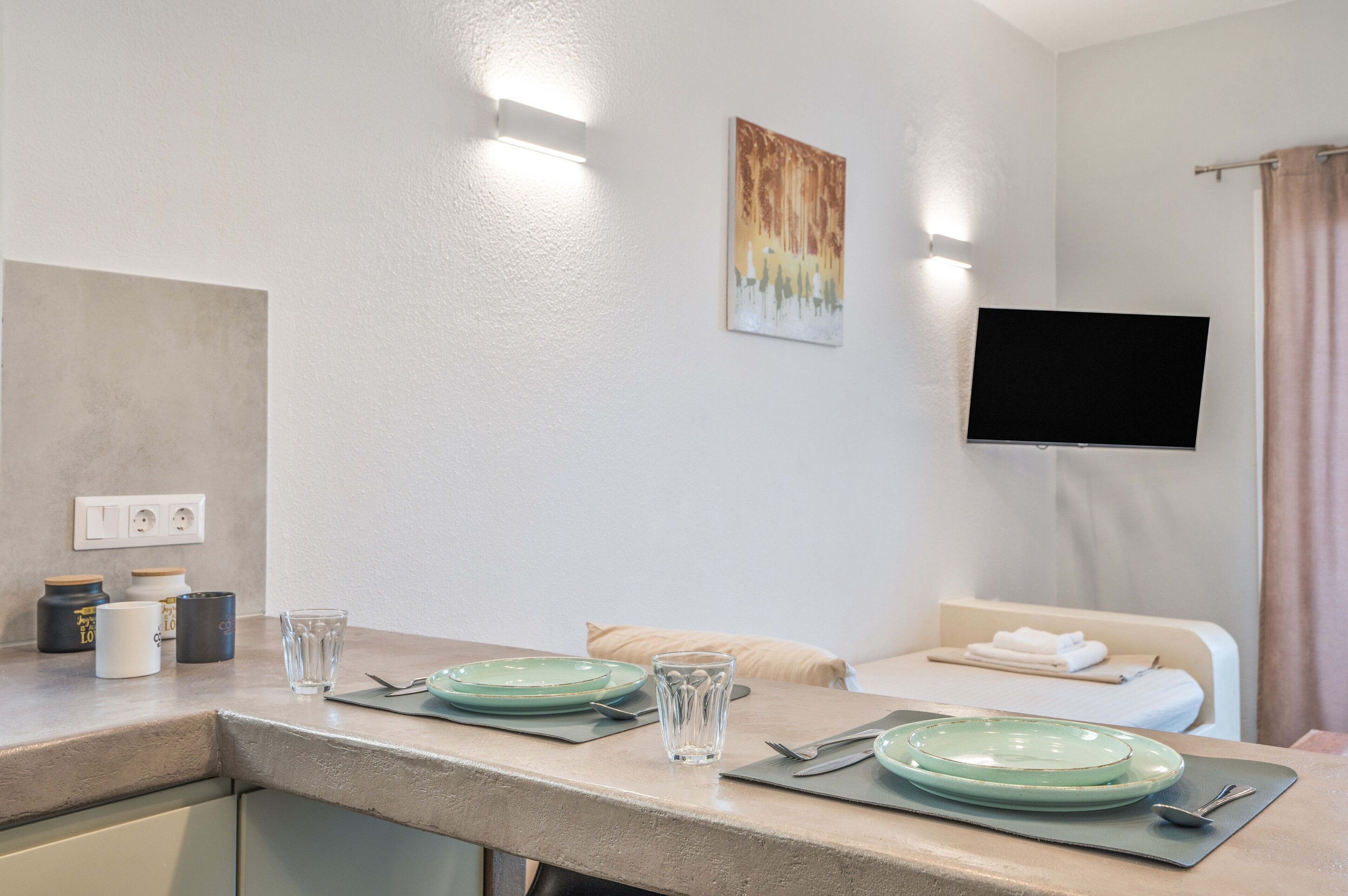 Ett hotellrum med en matplats, en platt-TV som är monterad på väggen och en säng med en beige sänggavel.