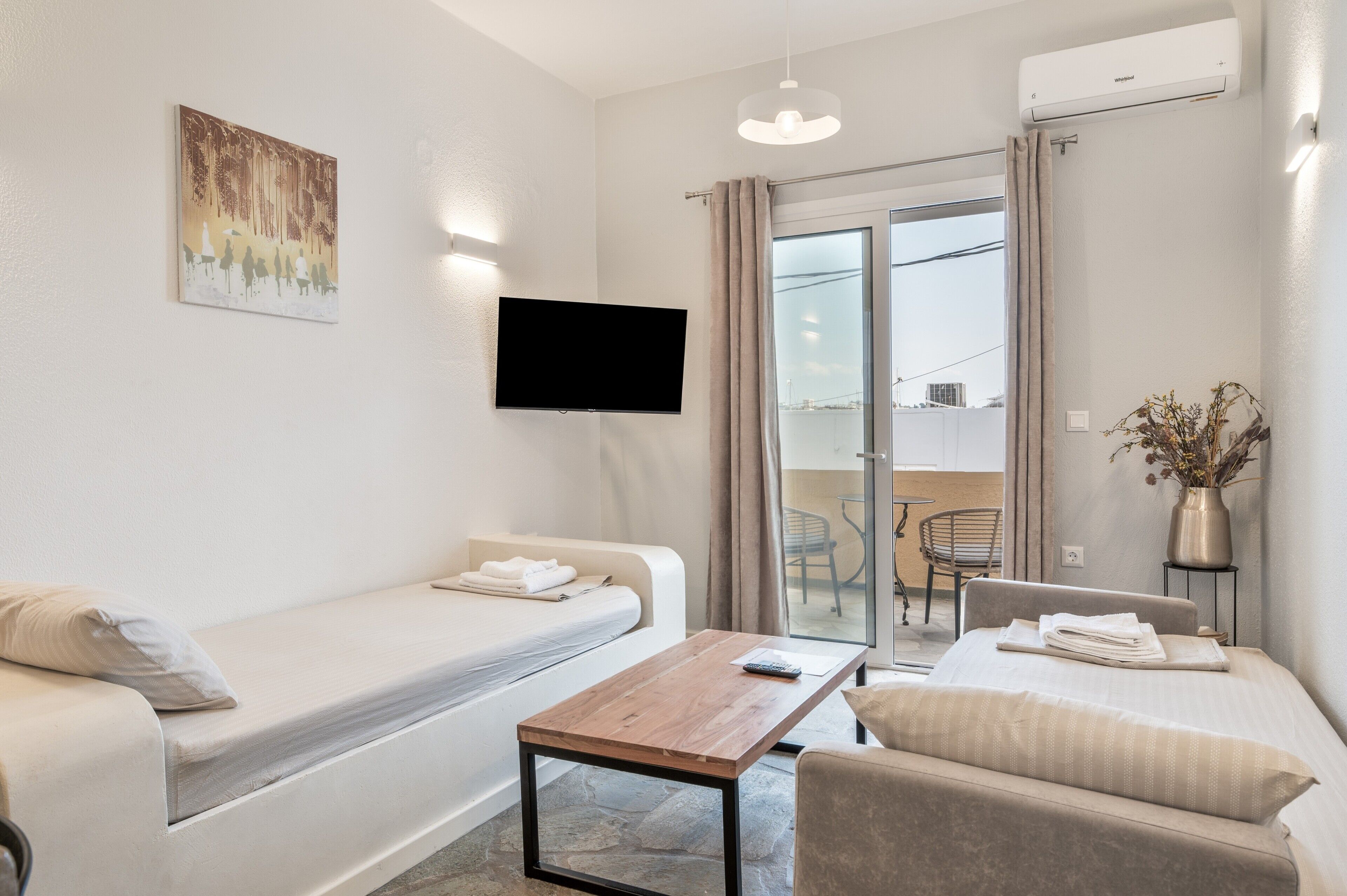 A modern hotel room with a sofa bed, a wooden table, a TV, and a balcony with a view.