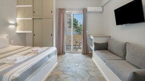 Habitación de hotel con cama, sofá, televisión y puerta corrediza de vidrio al balcón.