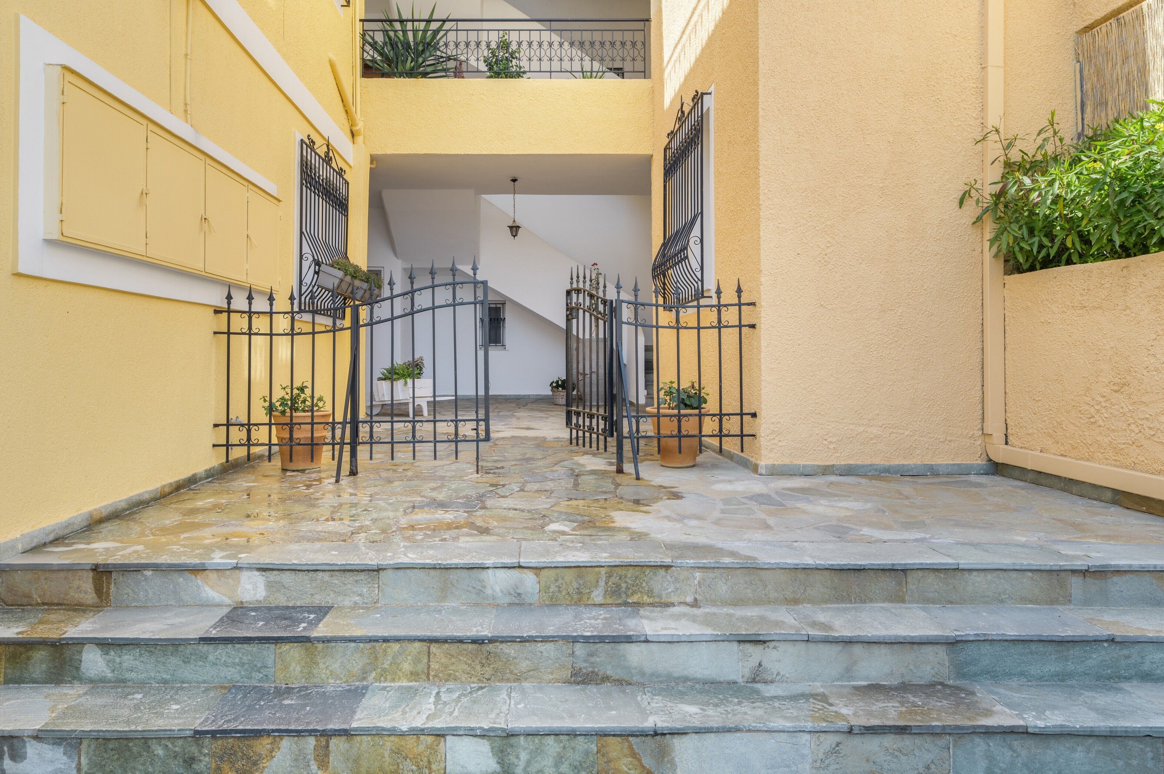 Eine Steintreppe führt zu einem Balkon mit Topfpflanzen und einem Metallgitter.