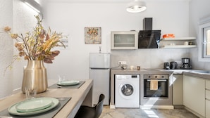 Una cocina compacta con lavadora, microondas y un pequeño comedor con un florero.