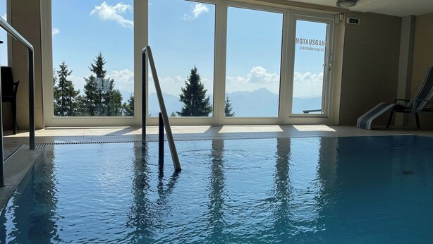Una piscina interior con vistas despejadas a árboles y montañas a través de amplios ventanales.