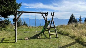 Un conjunto de columpios de madera con una escalera, con montañas y árboles de fondo.