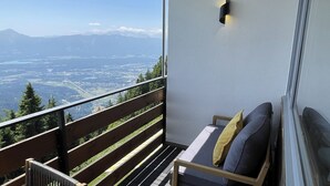 Un balcón con barandilla de madera, un banco acolchado y vistas a un paisaje montañoso.