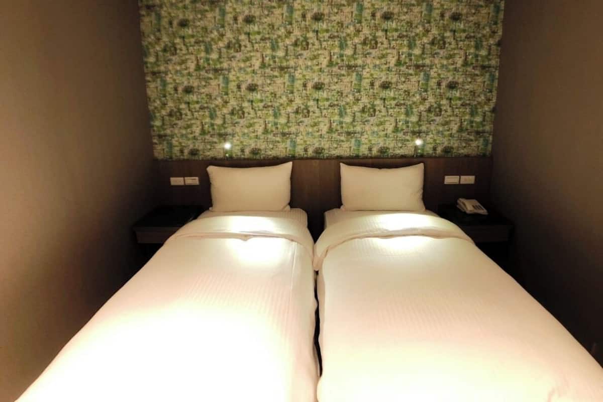 A hotel room with two single beds, a headboard with a patterned wallpaper, bedside tables with lamps, and a telephone.