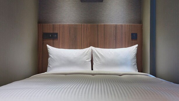 A neatly made bed with a striped bedspread and two pillows, set against a wooden headboard with a control panel on the left. - 128 INN- Self Check In (Taipei)