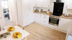 Una cocina moderna con armarios blancos, una campana extractora negra y un comedor con platos amarillos y copas de vino.