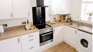 Cocina moderna con armarios blancos, una campana extractora negra, horno, lavadora y ventana que proporciona luz natural.