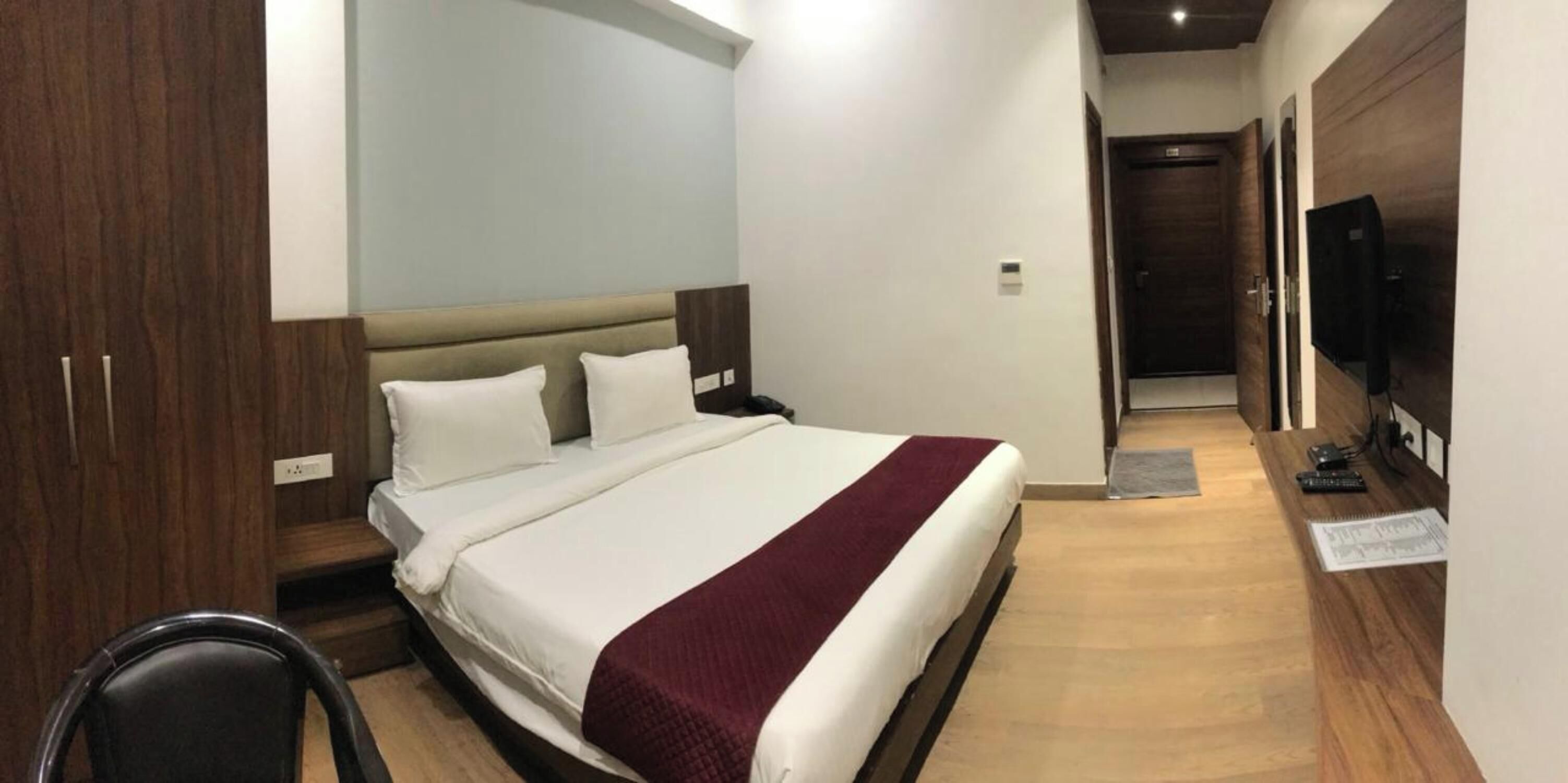 Ein Hotelzimmer mit einem Bett, einem Schreibtisch, einem Sessel, einem Fernseher und einem Holzschrank.