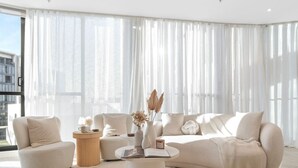 A modern living room with a large sectional sofa, a round coffee table, and a side table. - Bouclé Haven | 2BR, Sunset Skyline Views + Parking (Wentworth Point)