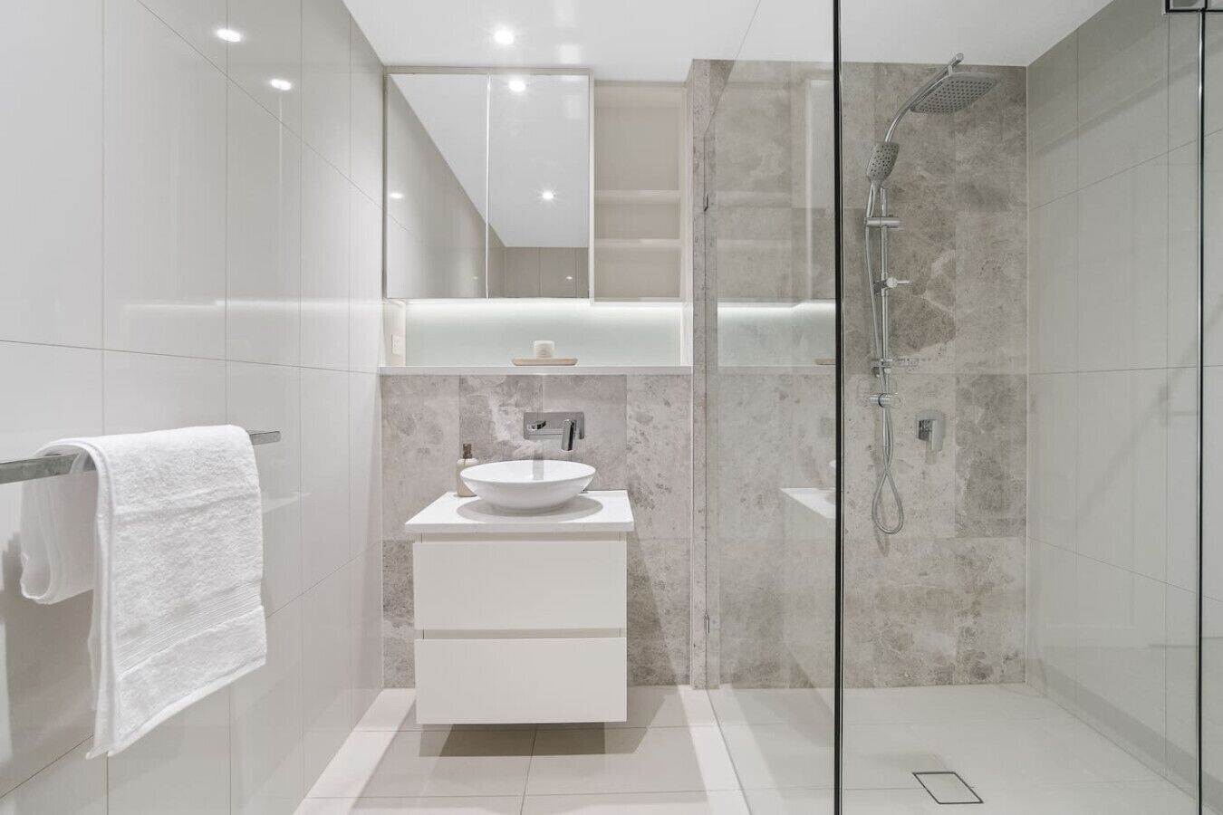 Een moderne badkamer met een douche met glazen wand, een witte wastafel en een spiegel erboven.