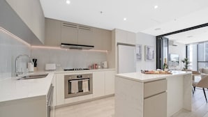 A modern kitchen with a central island, built-in oven, and stainless steel appliances. - Bouclé Haven | 2BR, Sunset Skyline Views + Parking (Wentworth Point)