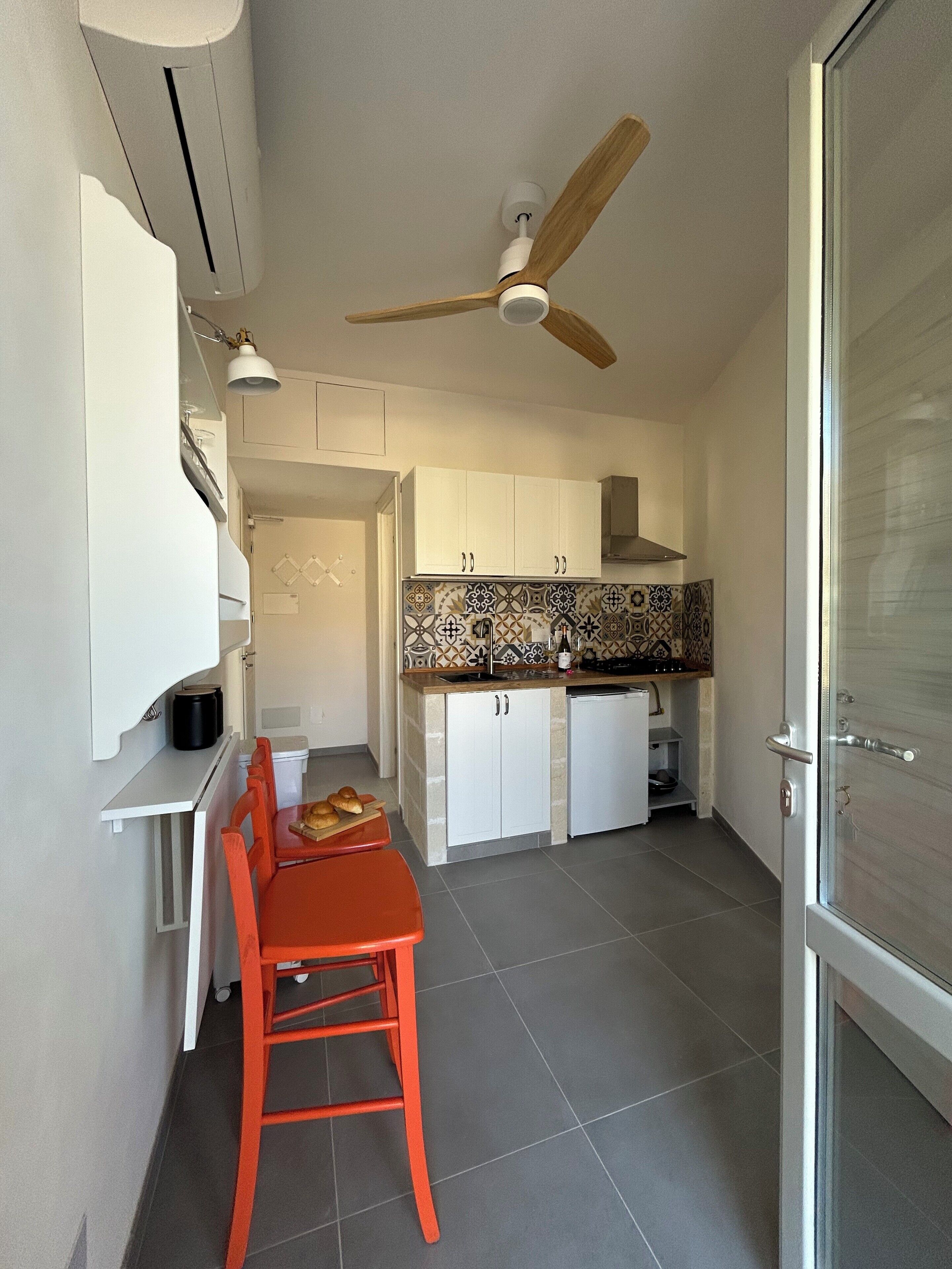 A compact kitchen with white cabinets, a tiled backsplash, and a ceiling fan.
