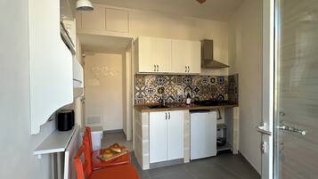 A compact kitchen with white cabinets, a tiled backsplash, and a ceiling fan.