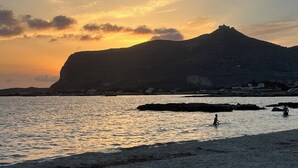 Eine Küstenlandschaft mit einem Berg, ruhigem Meer und einer Person im Wasser.