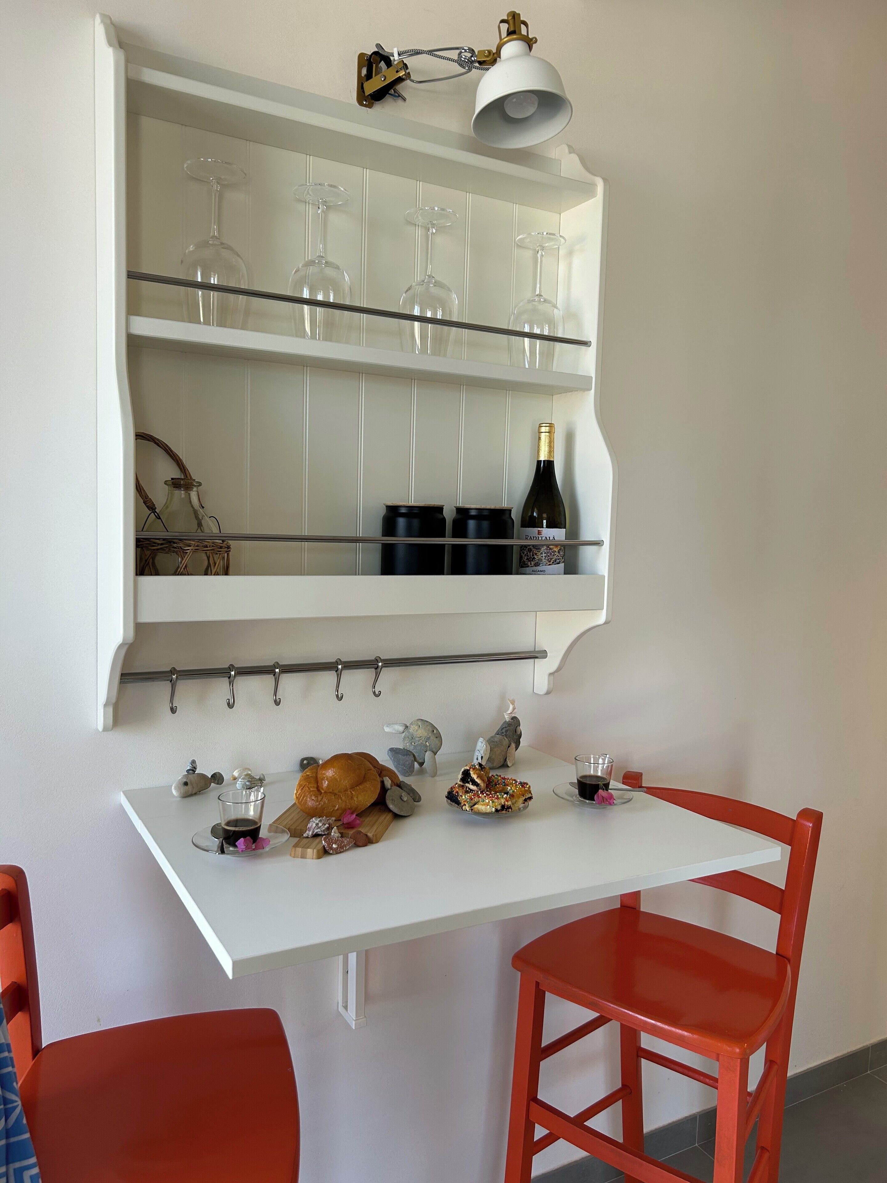 Een eethoek met een witte tafel, rode stoelen, een wijnrek met glazen en een fles wijn.