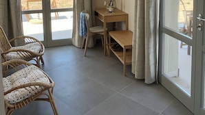 Ein Zimmer mit Schreibtisch aus Holz, einem Sessel, einem an der Wand befestigten Fernseher und Blick auf den Strand durch große Glasüren.