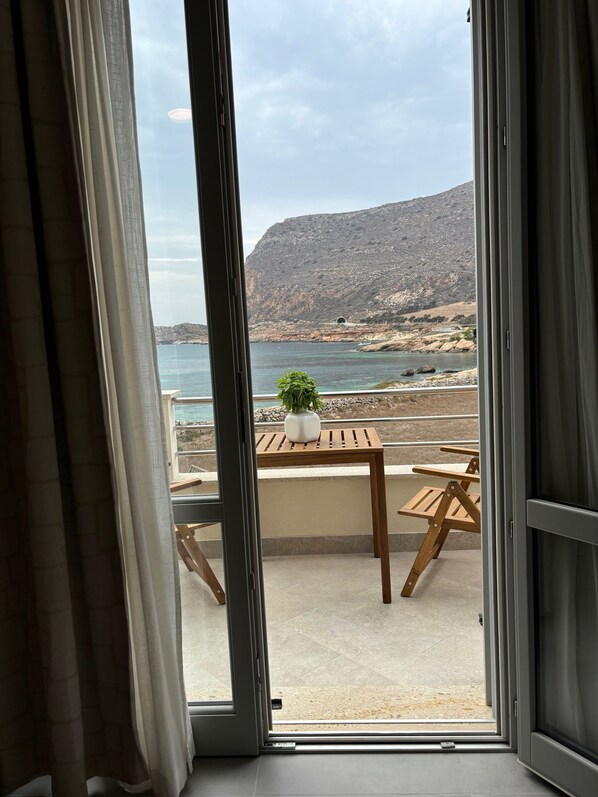 An open sliding door leading to a balcony with a view of a coastal landscape, a wooden table, and a potted plant. - ReMare Favignana (Favignana)