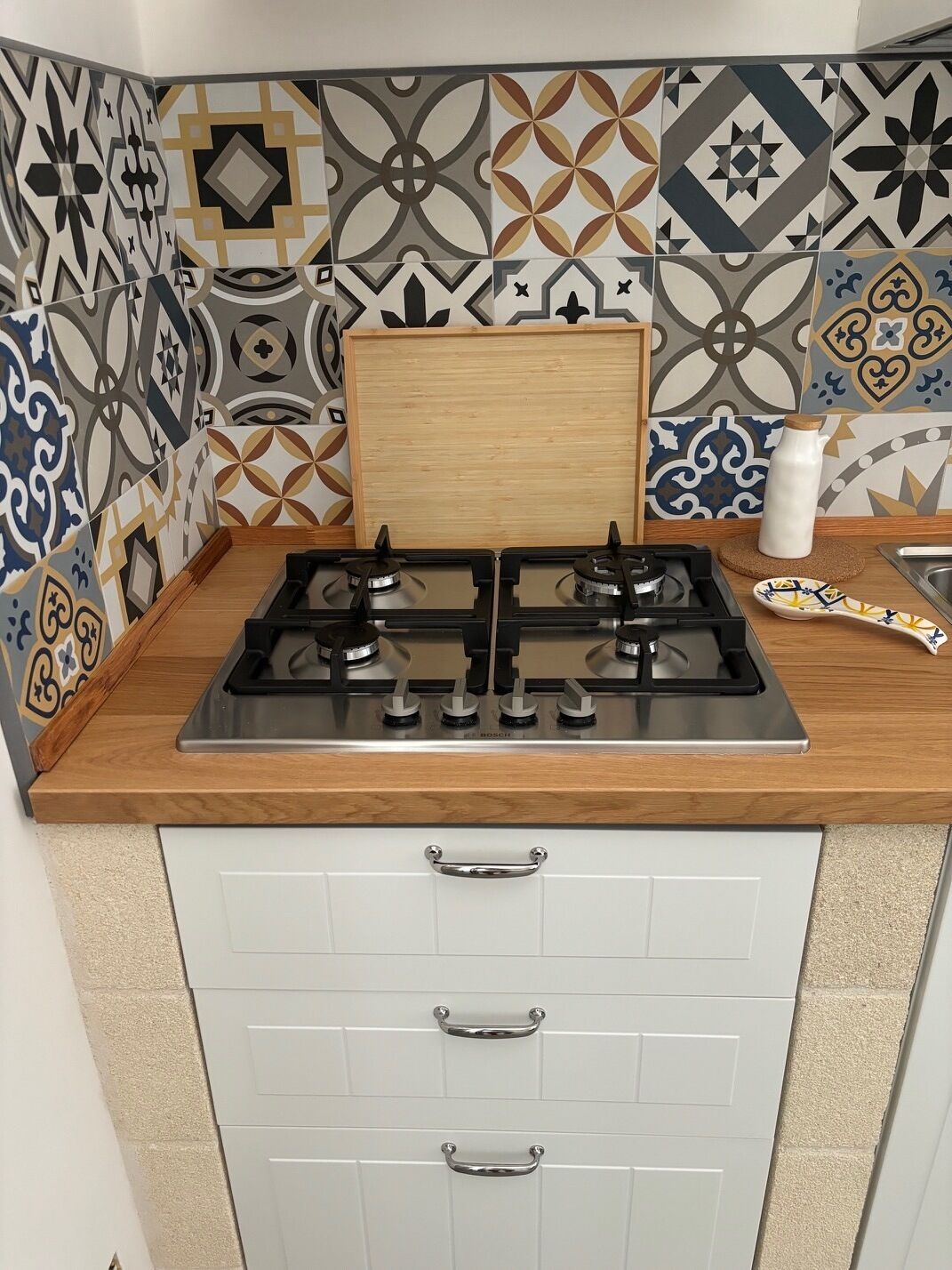 Une cuisine équipée d’une cuisinière à gaz, de deux tiroirs et de carreaux décoratifs sur le plan de travail.
