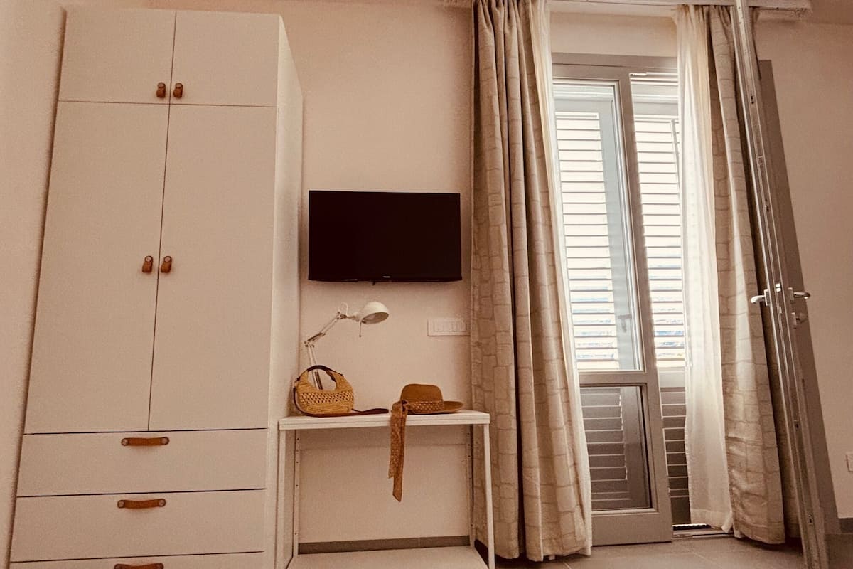 Une chambre avec une armoire, un téléviseur, une petite table avec une lampe et une porte coulissante avec des rideaux.