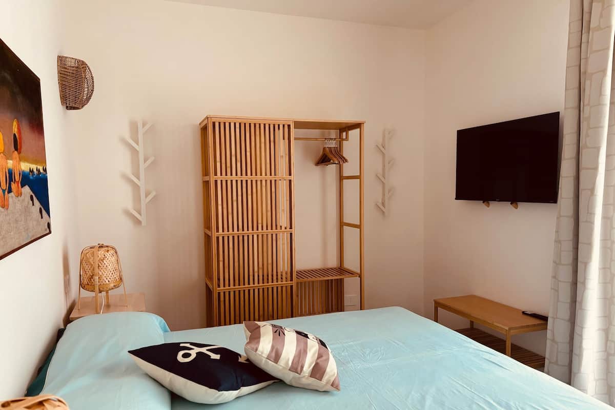 Une chambre à coucher avec un lit, une armoire en bois, une télévision et un tableau accroché au mur.