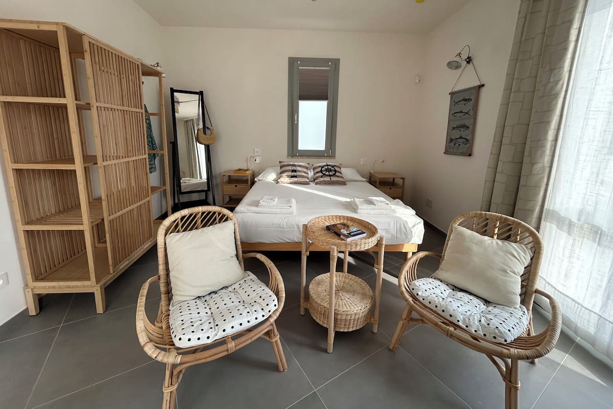 Une chambre à coucher comprenant un lit, deux fauteuils en osier, une armoire en bois, un miroir et un ventilateur de plafond.