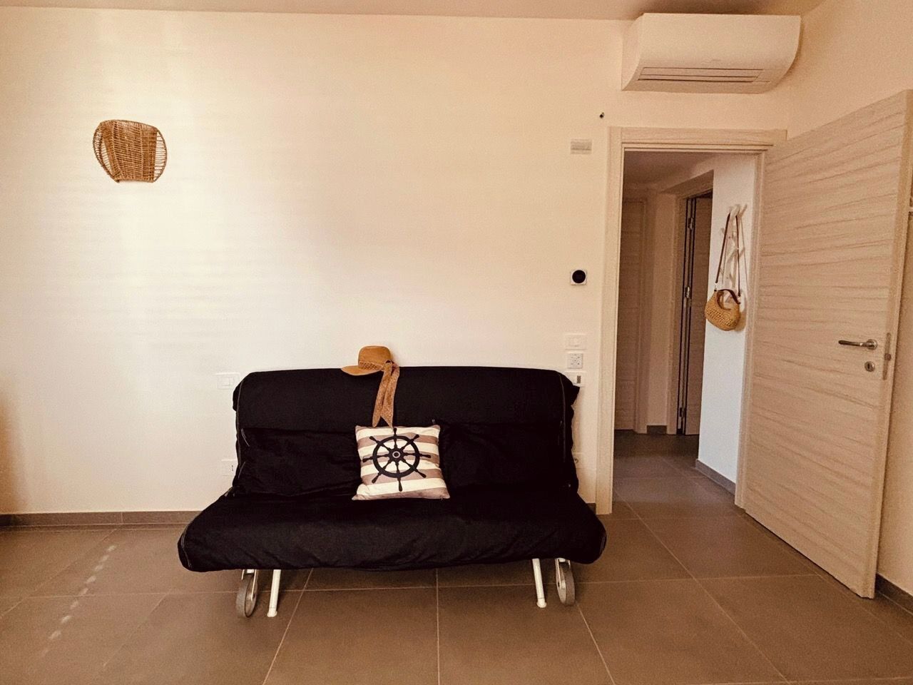 A black sofa with a star wheel pillow, a hat, and a woven basket on the wall.
