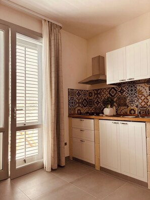 Una cucina con mobili bianchi, un backsplash decorato e una finestra con tende.
