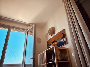 Ein Zimmer mit einem großen Fenster, einem Gemälde und einem Regal mit Gegenständen.