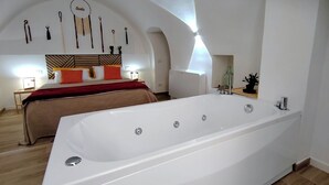 Un dormitorio moderno con una bañera blanca grande, una cama con ropa de cama naranja y blanca, y un diseño de techo curvo y original.
