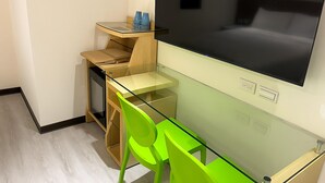 Ett kompakt rum med ett glasbord, en stor platt-TV och en ljusgrön stol.