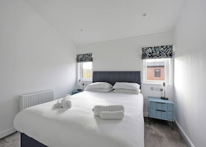 Une chambre à coucher avec un lit, deux tables de chevet, une fenêtre donnant sur un paysage agréable et un radiateur.