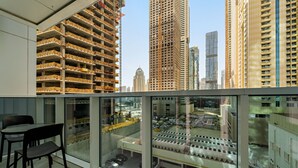 A high-rise building with multiple floors, a glass balcony with a table and chairs, and a view of a busy street with cars and other buildings. - Stylish 2BR in Dubai Marina Near the Beach (Dubai)