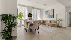 A modern living room with a dining area, a sofa, a coffee table, and a painting on the wall. - Stylish 2BR in Dubai Marina Near the Beach (Dubai)
