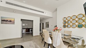 A modern dining area with a glass table, white chairs, and a decorative wall piece. - Stylish 2BR in Dubai Marina Near the Beach (Dubai)