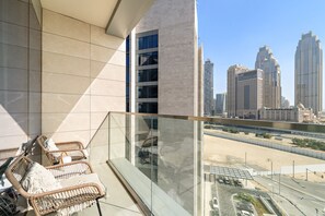 A balcony with wicker furniture, a glass railing, and a view of a cityscape with tall buildings. - Elegant Canal-Front 1 BD in a Prime Location (Dubai)