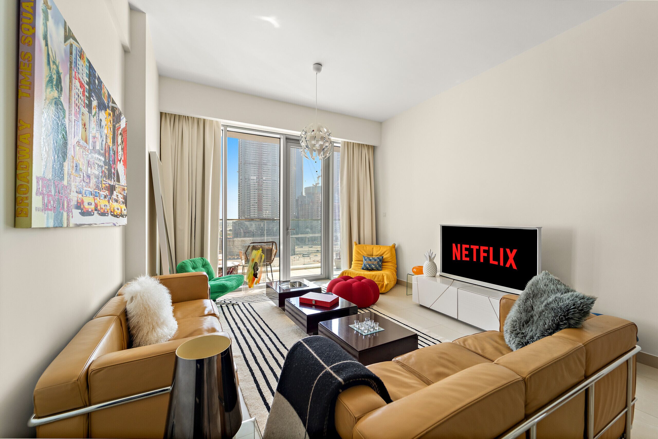 Moderni olohuone, jossa on nahkasohvat, suuri televisio, jossa näkyy Netflix, ja suuret ikkunat, joista avautuu näkymä kaupunkimaisemaan.