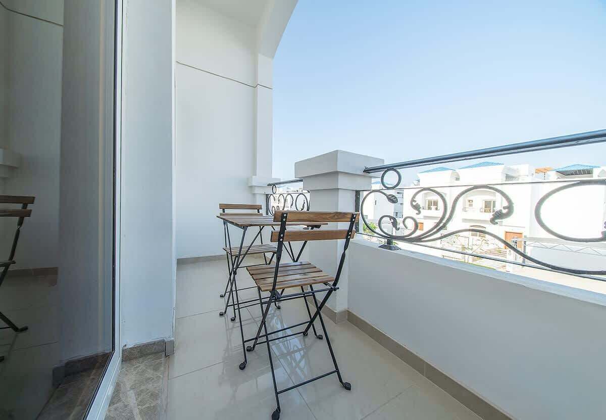 Een balkon met een metalen hekwerk, een houten tafel en een stoel.