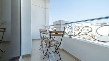 Een balkon met een metalen hekwerk, een houten tafel en een stoel.