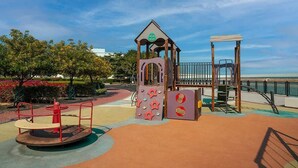 A playground with a climbing structure, a swing set, and a merry-go-round. - Elegant Waterfront Villa W Sunset Terrace (Ajmal Makan)