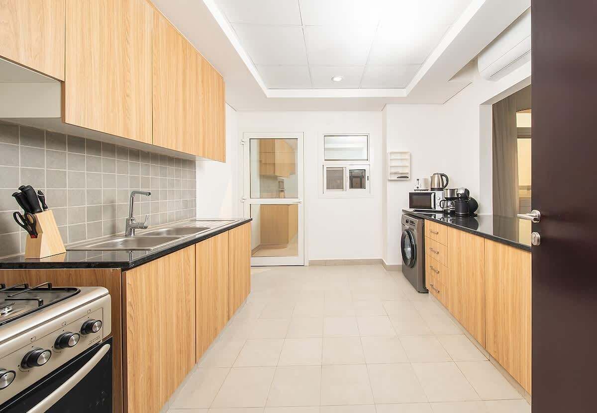 Een moderne keuken met houten kastjes, een gasfornuis, een spoelbak en een wasmachine.