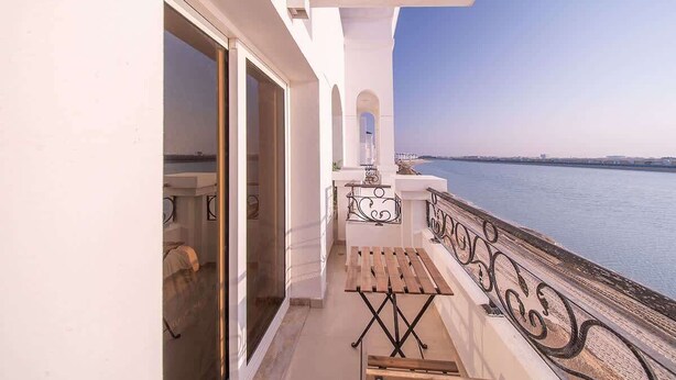 A balcony with a view of the sea, a wooden table, and a white wall. - Elegant Waterfront Villa W Sunset Terrace (Ajmal Makan)