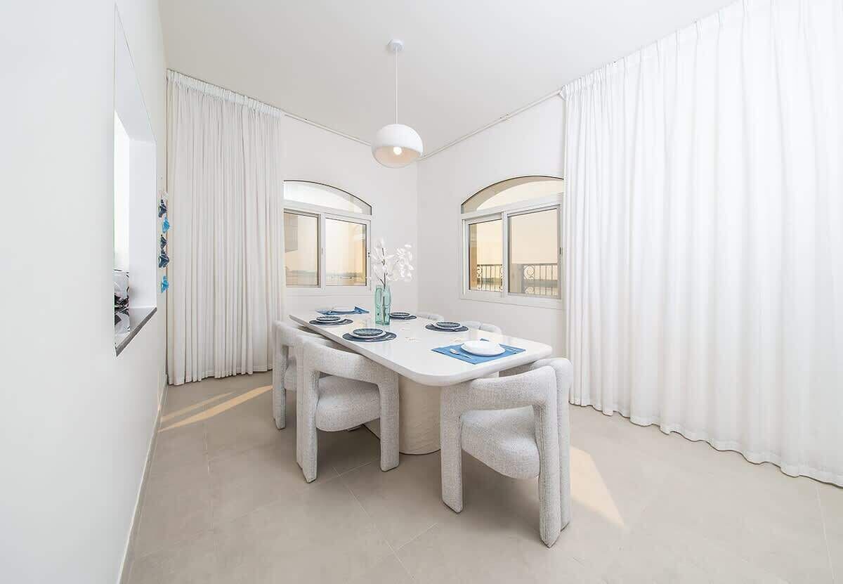Een moderne eethoek met een witte tafel gedekt voor vier personen, twee stoelen en een hanglamp.