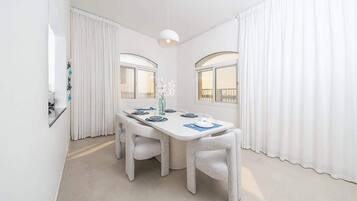 Een moderne eethoek met een witte tafel gedekt voor vier personen, twee stoelen en een hanglamp.