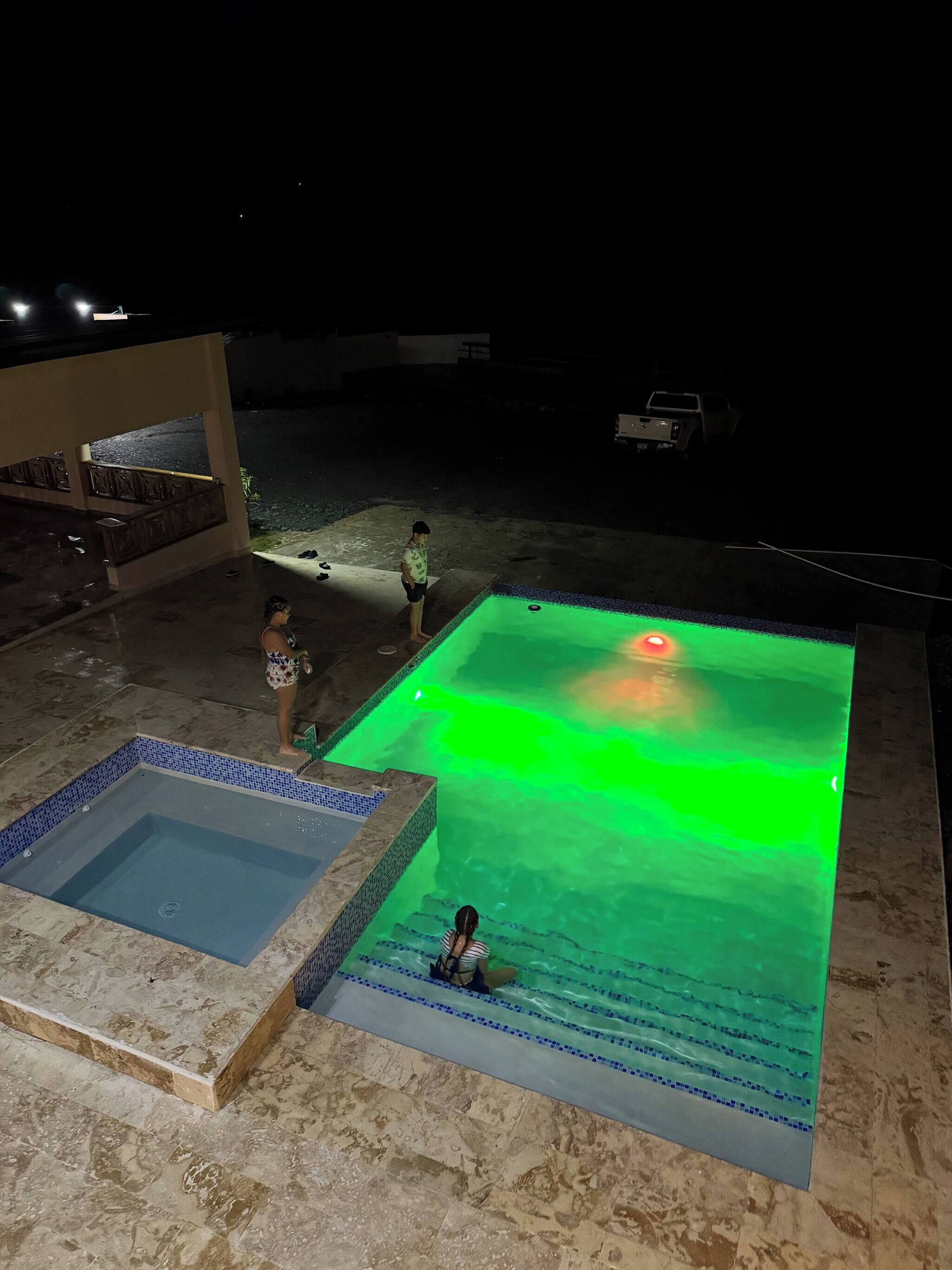 A swimming pool with a green light feature, a smaller adjacent pool, and a person sitting in the water.
