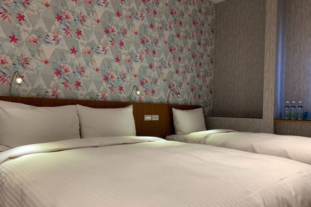 A hotel room with two beds, a floral-patterned wall, and a wooden headboard.